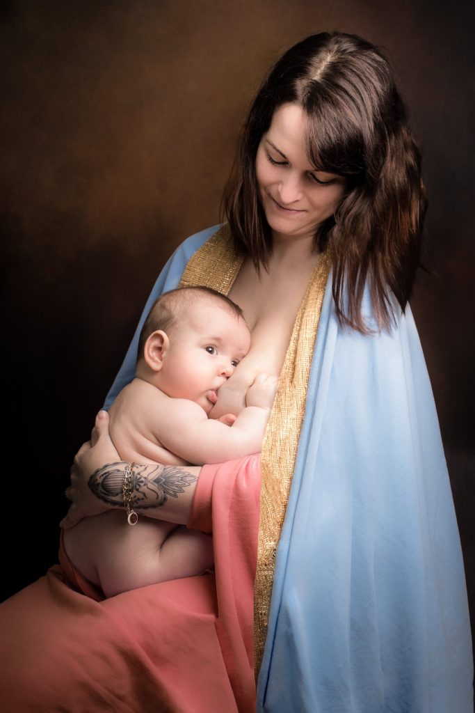 Séance photo bébé & moi au studio photo Ophélie Bajeux Photographie. Petite garçon dans les bras de sa maman, dans un style artistique. Photo montrant un allaitement dans un style de tableau de la madone.