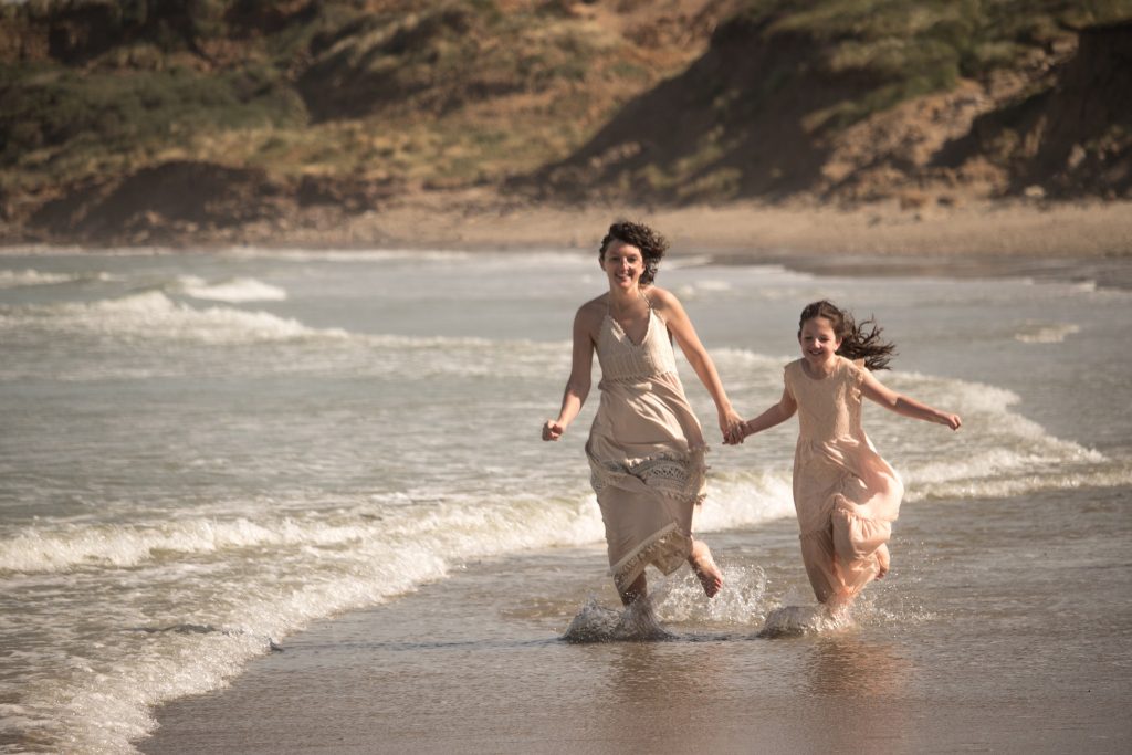 Portrait mère et fille fait à l'extérieur sur la côte de Wimereux entrain de courir les pieds dans l'eau.