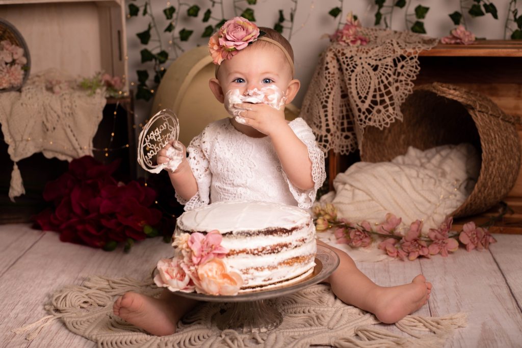 Séance bébé smash cake chez Ophélie Bajeux photographie. Petite fille de aux yeux bleus mangeant un gâteau smash cake.