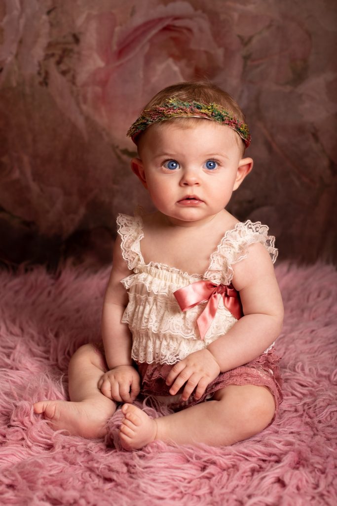Séance bébé 6/9mois chez Ophélie Bajeux photographie. Petite fille de aux yeux bleus sur un fond rose.