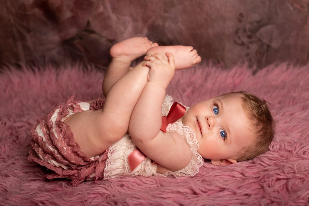 Séance bébé 6/9mois chez Ophélie Bajeux photographie. Petite fille de aux yeux bleus sur un fond rose.
