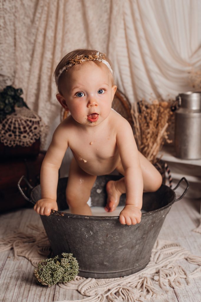 Séance bébé smash cake chez Ophélie Bajeux photographie. Petite fille de aux yeux bleus dans un bain de lait après une séance photo avec un gâteau smash cake.