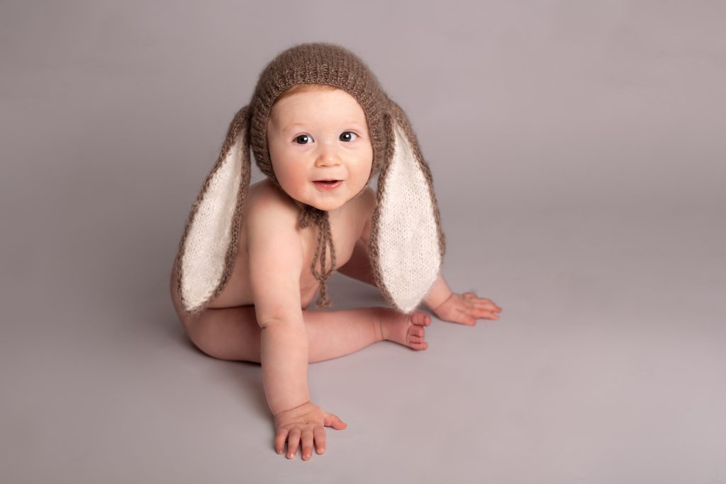 Séance bébé 6/9mois chez Ophélie Bajeux photographie. Petit garçon avec bonnet lapin, sur un fond blanc.